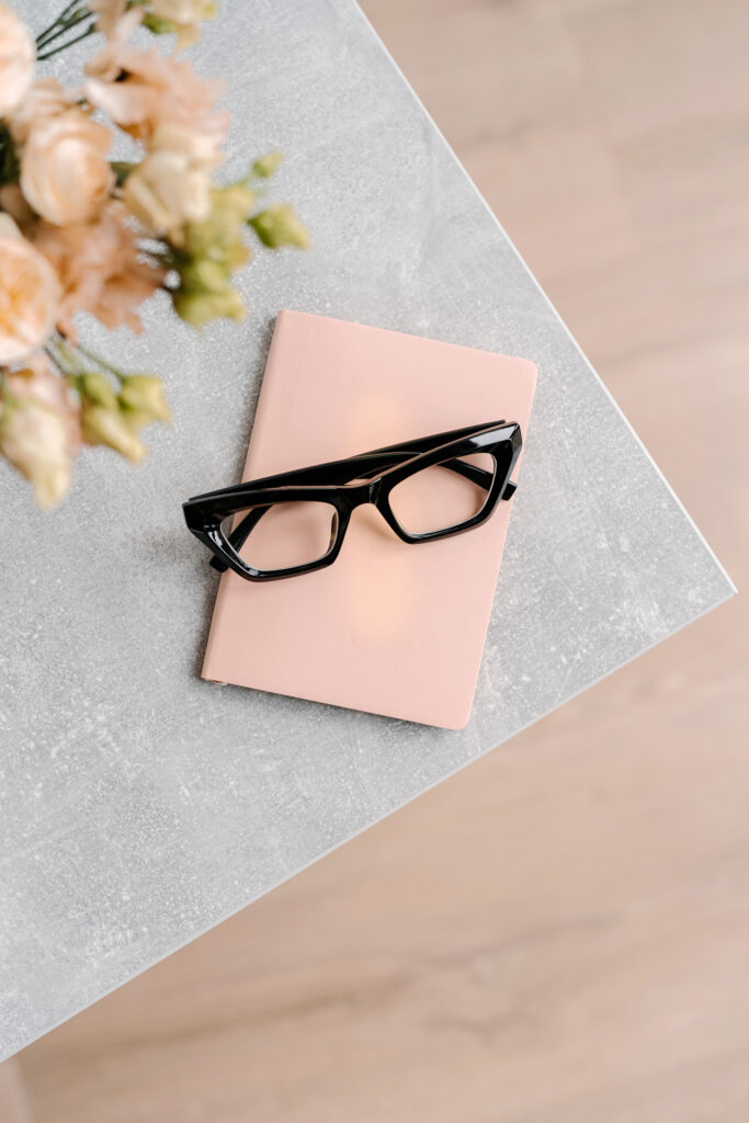 Reading glasses on note paper with flowers in background on desk